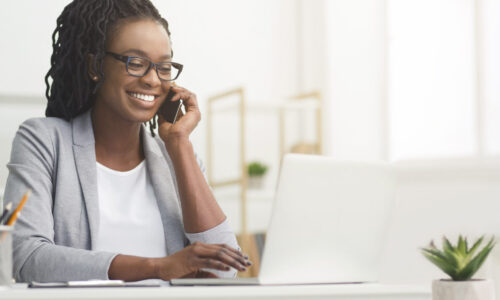 Lady Boss. Afro Businesswoman Talking On Cellphone While Working On Laptop In Modern Office, Wide Horizontal Banner, Panorama With Free Space